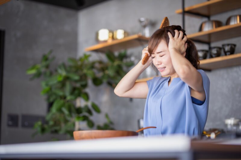 自宅のキッチンで頭を抱える女性